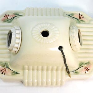 Puede incluir: Luminaria de techo vintage de color crema con dos portalámparas. La luminaria tiene forma rectangular con un diseño acanalado y detalles florales en rosa y verde. Una cadena decorativa cuelga del centro.