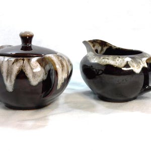May include: A brown and white ceramic sugar bowl and creamer set. The set has a drip glaze design.