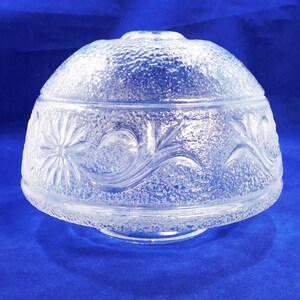 May include: Clear glass lampshade with a textured surface and a floral design. The shade has a rounded top and a flat bottom.