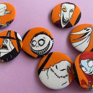 Puede incluir: Conjunto de siete botones redondos de tela naranja y negro con personajes de la película Pesadilla antes de Navidad. Los personajes incluyen a Jack Skellington, Sally, Oogie Boogie, Zero y el alcalde.