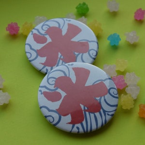 May include: Two round white and blue pins with a red Japanese character for "ice" on a yellow background. The pins are surrounded by small colorful candies.