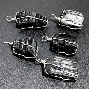 May include: Five black tourmaline crystal pendants wrapped in silver wire. The crystals are all different shapes and sizes.