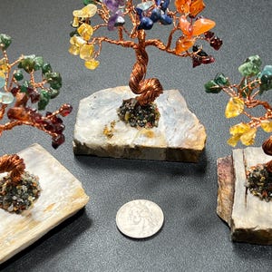 Peut inclure: Trois petits arbres en fil de fer enroul&eacute; avec des pierres pr&eacute;cieuses color&eacute;es sur chaque branche. Les arbres sont sur de petites bases en pierre plates, grises et blanches. Une pi&egrave;ce de monnaie am&eacute;ricaine de 25 cents est repr&eacute;sent&eacute;e &agrave; titre de comparaison.