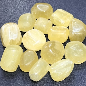 May include: A collection of yellow tumbled stones. The stones are smooth and polished, with a variety of shapes and sizes.