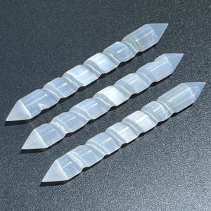 May include: Three white selenite wands with a spiral pattern. The wands are pointed at one end and have a smooth, polished surface.