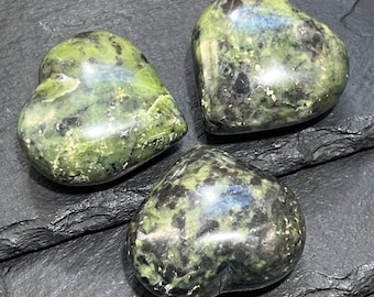 Puede incluir: Tres piedras pulidas en forma de corazón con un patrón moteado de verde bosque profundo, oliva e inclusiones negras. Cada piedra tiene una superficie lisa y reflectante con variaciones sutiles de color y textura en las formas redondeadas.
