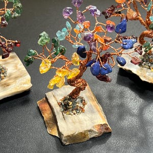 Peut inclure: Un arbre en cristal arc-en-ciel avec des branches en fil de cuivre et une vari&eacute;t&eacute; de pierres pr&eacute;cieuses color&eacute;es. L'arbre est pr&eacute;sent&eacute; sur une base en pierre naturelle.