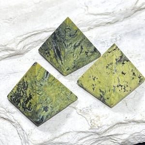 May include: Three pyramid-shaped objects crafted from a lime green stone featuring intricate black veining and dark mineral inclusions. Each piece displays a smooth, polished surface with a distinct pattern of natural cracks and color variations.