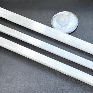Peut inclure: Trois baguettes de cristal de sélénite blanches et une pierre d'agate ronde et polie. Les baguettes de sélénite sont rectangulaires et de longueurs variables. La pierre d'agate est blanche et grise avec un motif circulaire.