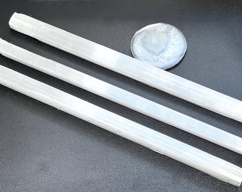 May include: Three white selenite crystal wands and a round, polished agate stone. The selenite wands are rectangular and vary in length. The agate stone is white and gray with a circular pattern.