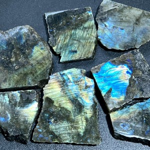 Puede incluir: Una colección de piezas de cristal de labradorita con tonalidades iridiscentes azules, verdes y doradas. Las piedras talladas en bruto tienen un aspecto natural y crudo.