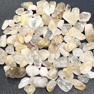 May include: A collection of small, tumbled, clear quartz stones with golden rutilated inclusions. The stones are various shapes and sizes, and have a natural, polished finish.
