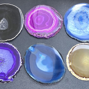 May include: Six agate coasters in various colors, including black, purple, blue, and brown. The coasters are round and have a natural, polished finish.