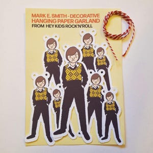 Può includere: Una ghirlanda decorativa di carta da appendere con diverse figure fustellate di Mark E. Smith che indossa un gilet a rombi gialli e neri e pantaloni neri. Il set include uno spago da cucina rosso e bianco e un cartoncino giallo con del testo.