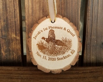 May include: A round wooden ornament with a brown ribbon. The ornament is engraved with the text "Jacob's 1st Pheasant & Quail Nov. 15, 2020 Stockton, KS" and an image of two birds.