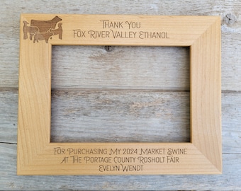 May include: A wooden picture frame with an engraved message thanking Fox River Valley Ethanol for purchasing a 2024 market swine at the Portage County Rosholt Fair. The frame features a silhouette of a pig and other livestock.