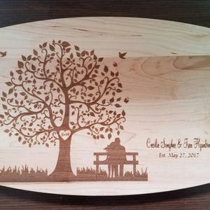 Könnte beinhalten: Ein Schneidebrett aus Holz mit einem lasergravierten Design eines Baumes mit einem Herzen an der Basis. Der Baum ist von Blättern und Vögeln umgeben. Der Text "Cecilia Jonhson & Evan Higuain Est. May 27, 2017" ist unter dem Baum graviert.