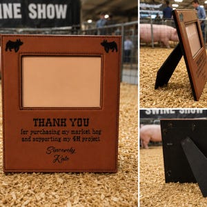Puede incluir: Un marco de fotos rectangular de color marrón con aspecto de cuero y dos siluetas de cerdos negras en las esquinas superiores. El texto dice: THANK YOU for purchasing my market hog and supporting my 4H project. Sincerely, Kate. Incluye soporte trasero.
