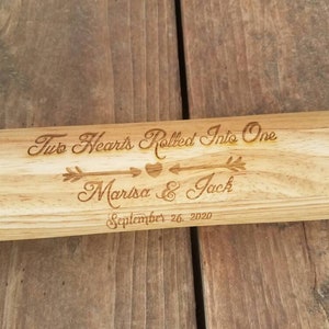 May include: A wooden baseball bat with the text "Two Hearts Rolled Into One" engraved on it. An arrow with a heart points to the names "Marisa & Jack" and the date "September 26, 2020".