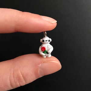 May include: A white robot charm with a red rose, holding the rose in its hands. The charm is made of polymer clay and has a silver jump ring.