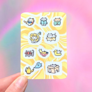 May include: A sticker sheet with cartoon cat illustrations. The cats are shown in different scenarios, including reading, wearing clothes, or in a box. The background is yellow with a swirl pattern.