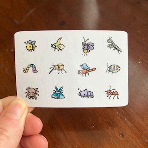 May include: A sheet of white stickers featuring colorful cartoon insects. The stickers include a bee, a caterpillar, a dragonfly, and other bugs. The illustrations are in a simple, hand-drawn style with black outlines.