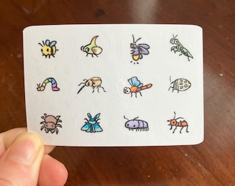 Puede incluir: Una hoja de pegatinas blancas con insectos de dibujos animados coloridos. Las pegatinas incluyen una abeja, una oruga, una libélula y otros insectos. Las ilustraciones son de estilo sencillo, dibujado a mano con contornos negros.