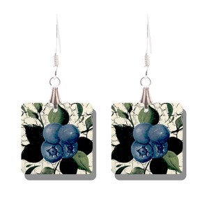 Peut inclure: Une paire de boucles d'oreilles carrées avec un motif de myrtilles. Chaque boucle d'oreille présente un groupe de myrtilles bleues avec des feuilles vertes et un fond noir sur un carré crème. Les boucles ont des crochets argentés.