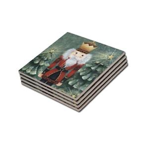 May include: Set of four square ceramic coasters featuring a whimsical illustration of a nutcracker standing in front of a green Christmas tree with gold stars. The nutcracker is wearing a red and black uniform with a gold crown.