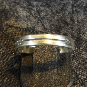 May include: A silver band ring with a thin line and an arrow design.