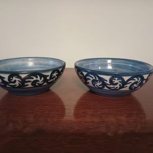 Puede incluir: Dos cuencos pequeños de cerámica azul y blanca con un patrón de espiral. Los cuencos están sobre una superficie de madera oscura.