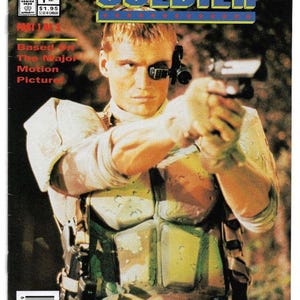 May include: A comic book cover for "Universal Soldier" featuring a man in military attire aiming a handgun. The title is in blue and yellow block letters. The cover includes the text "Based On The Major Motion Picture."