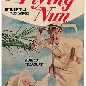 May include: A vintage comic book cover featuring a nun in a white habit with a large white hat. The title of the comic is "The Flying Nun" and the text "Sister Bertille Faces Danger! Buried Treasure?" is also visible. The comic book cover is in a blue and green color scheme.