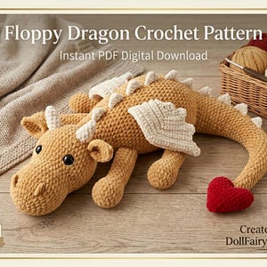 Op de afbeelding: Een gehaakt draakspeelgoed in bruintinten, met witte accenten op de vleugels en hoorns, en een rood hartvormig staartje. De tekst "Floppy Dragon Crochet Pattern" en "Instant PDF Digital Download" staan bovenaan.