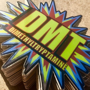 Pode incluir: Uma pilha de adesivos coloridos com um design de estrela. Os adesivos apresentam o texto "DMT" em letras amarelas com contorno vermelho e as palavras "DIMETHYLTRYPTAMINE" em letras vermelhas.