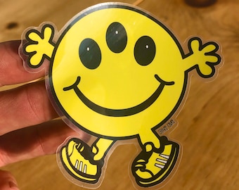 May include: Yellow smiley face sticker with three eyes and a big smile. The smiley face is wearing shoes and has arms and legs. The sticker says "Sh*z Owne" at the bottom.