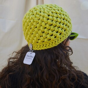 May include: A lime green crocheted beanie with a white tag that reads "Ollie Nash Yarn Works Handmade Crochet & Knits".