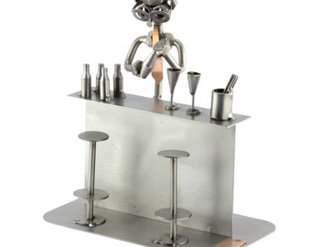 May include: A metal sculpture of a bartender making a cocktail behind a bar with two stools. The bartender is made of nuts and bolts and has a tie. The bar is made of metal and has a copper plate on the bottom.