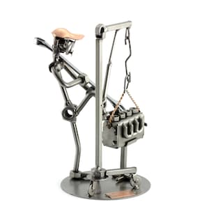 Puede incluir: Una figurita de metal de un trabajador levantando un motor de coche con una grúa. El trabajador está hecho de varias piezas de metal, incluyendo llaves, tuercas y tornillos. La grúa también está hecha de metal y tiene una cadena y un gancho. El motor está hecho de metal y tiene un diseño detallado.
