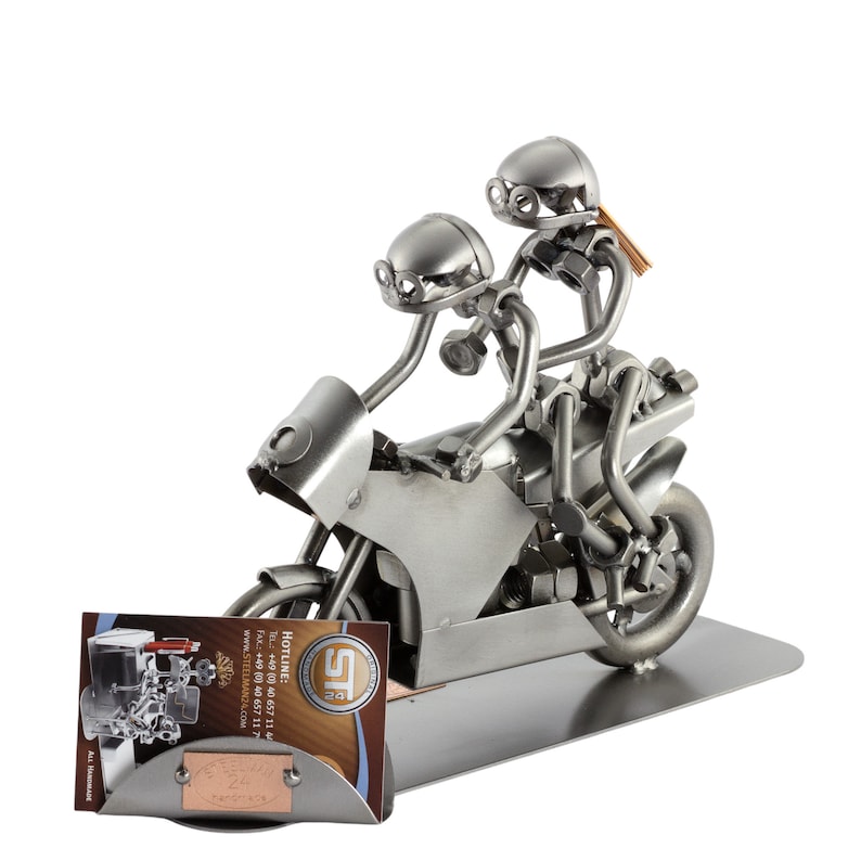 May include: A metal sculpture of two figures riding a motorcycle. The figures are made of nuts, bolts, and other metal pieces. The motorcycle is also made of metal and has a detailed design. The sculpture is on a metal base.