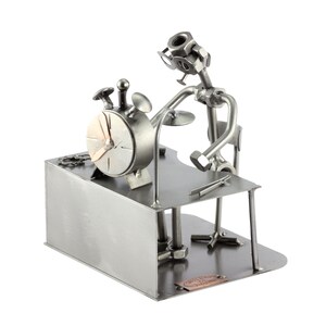 Peut inclure: Sculpture métallique artisanale représentant une personne jouant de la batterie. La sculpture est faite d'écrous, de boulons et d'autres pièces métalliques. Une horloge est posée sur le bureau. La sculpture est de couleur argentée et a une esthétique industrielle unique.