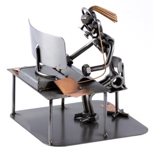 Può includere: Una scultura in metallo di una persona che lavora a una scrivania con un computer. La scultura è realizzata con vari pezzi di metallo, tra cui dadi, bulloni e filo. La persona è seduta a una scrivania con un monitor di computer e un piccolo pezzo di metallo color rame.