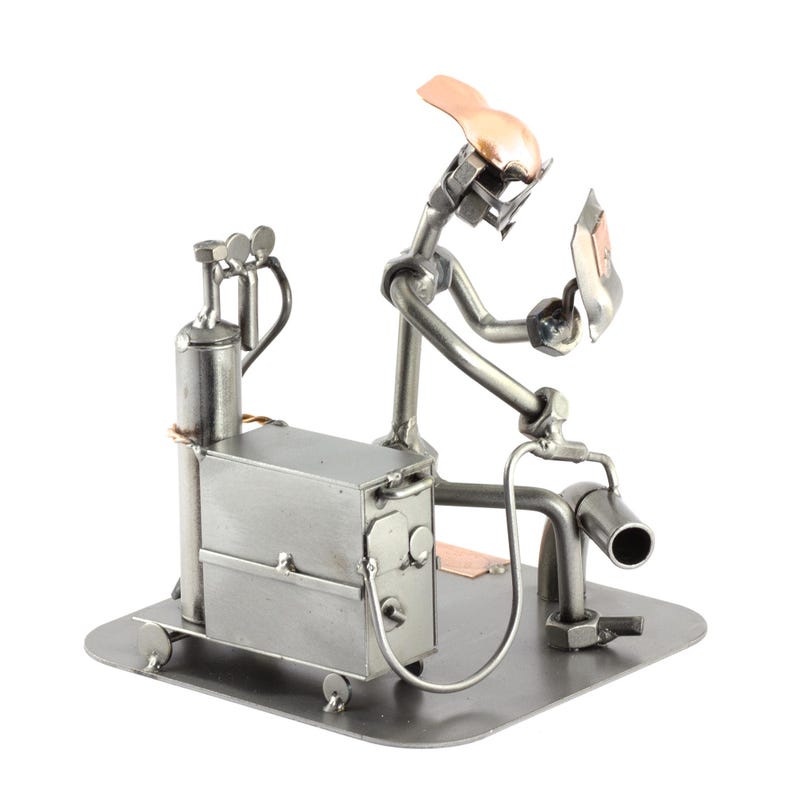 May include: A metal figurine of a welder working on a welding machine. The figurine is made of various metal pieces, including nuts, bolts, and screws. The welder is wearing a welding mask and holding a welding torch. The welding machine is on wheels and has a tank on the side.