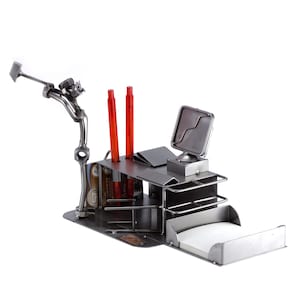 Könnte beinhalten: Ein einzigartiger Schreibtisch-Organizer aus Metall mit einer Golferfigur, zwei roten Stiften, einem kleinen Monitor und einem Notizblockhalter. Der Organizer hat ein modernes, industrielles Design.