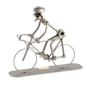Puede incluir: Una escultura de metal de un ciclista montando una bicicleta. La escultura está hecha de tuercas, tornillos y otras piezas de metal. El ciclista lleva un casco y tiene una expresión decidida en su rostro.