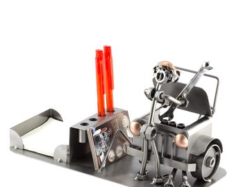 May include: A metal desk organizer shaped like a jeep with a figure of a person behind the wheel. The jeep has an open hood and the figure is holding a wrench. The organizer has a pen holder, a note pad holder, and a business card holder.