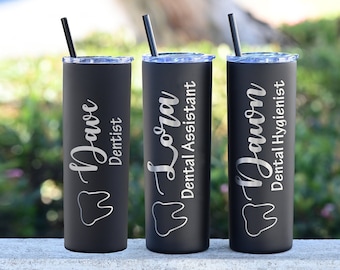 May include: Three black stainless steel tumblers with a tooth graphic and personalized names and job titles. The tumblers are "Dave Dentist", "Lori Dental Assistant", and "Dawn Dental Hygienist".
