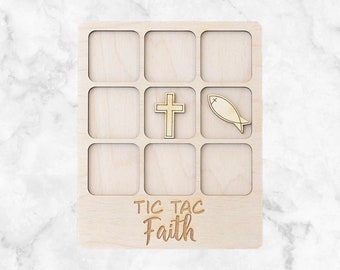 May include: Wooden Tic Tac Toe game with the words "Tic Tac Faith" engraved at the bottom. The game board has nine square spaces. The game pieces are a gold cross and a gold fish symbol.