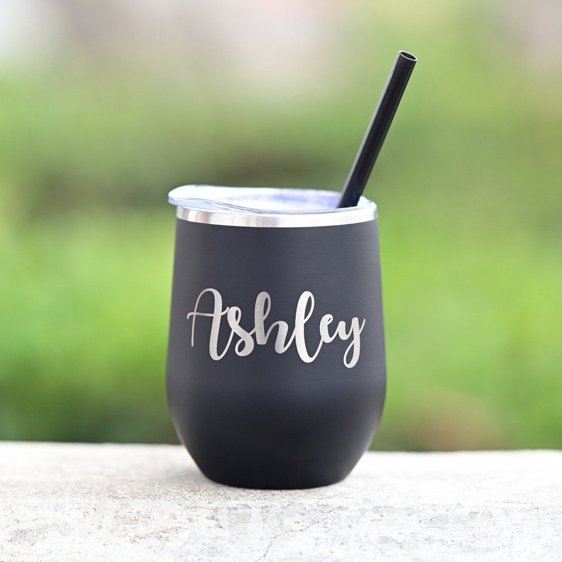 Puede incluir: Un vaso de vino de acero inoxidable negro con tapa y pajita. El vaso tiene el nombre "Ashley" grabado en el lateral.