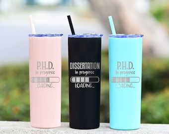 May include: Three stainless steel tumblers with lids and straws. The tumblers are pink, black, and blue. Each tumbler has a progress bar graphic with the text "P.H.D. In progress" or "DISSERTATION In progress" and "LOADING..."
